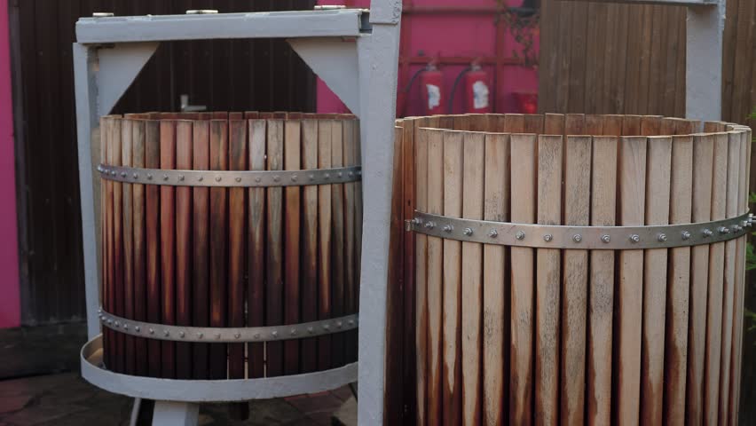 Wine manual press for crushing and pressing grapes at the winery. Tools for making and fermenting wine. Wooden barrels for pressing grapes.