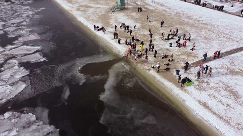 the drone flies over the hole in the winter river, the river is covered with ice, people enter the cold water, cross themselves and plunge headlong into the ice water three times
