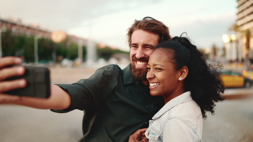 Closeup portrait of smiling interracial couple taking a selfie on urban city background. Close-up, man and woman video chatting using a mobile phone Royalty-Free Stock Footage #1098892165