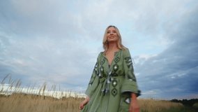 View of beautiful blond woman running through the wheat field at dawn, romantic mood, green embroidered dress, happy face, tender silhouette. Sunset with cloudy blue sky, out of the city. HQ 4k