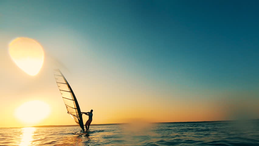 Sunset sea and a windsurfer managing a sailboard