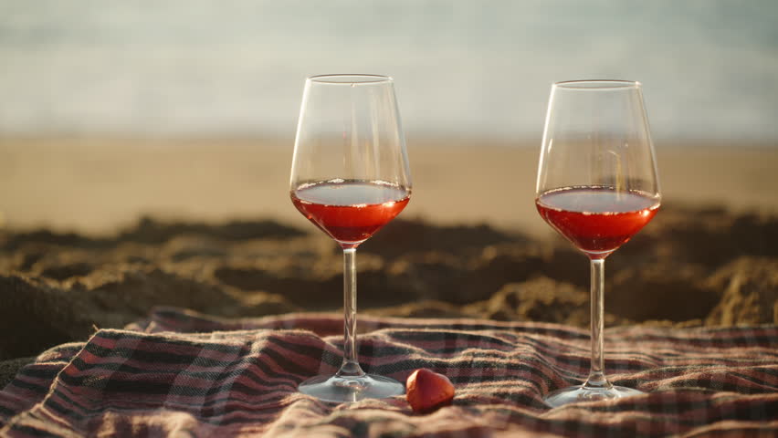 Two glasses of wine and sweets in the shape of a heart, on a plaid, A romantic sunrise on the seashore.