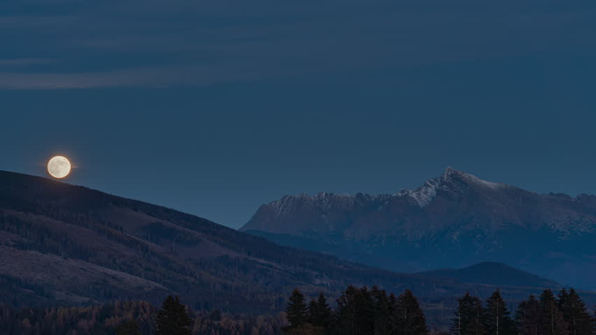 Full moon rising over mount Krivan peak - Slovak symbol - forest trees silhouettes in foreground, evening scene timelapse video