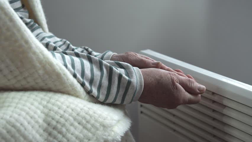 An elderly woman warms her cold hands over an electric heater. Cold season. Saving electricity. Energy crisis. Poor citizens. The predatory policy of the state | Shutterstock HD Video #1098904589
