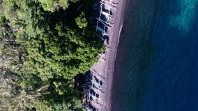 Vertical video of Black sand beach with traditional indonesian fishing boats and colorful water