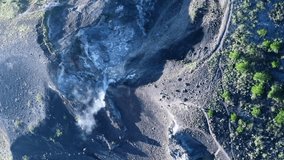Vertical video of Smoke coming out of volcano crater with people walking on the edge