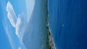 Vertical video of Coast of island with black sand beach and volcano erupting in background
