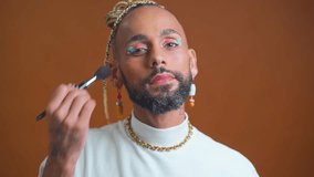 Homosexual man who applies powder to his face makeup brush. LGBT community with freedom for homosexuals. Black Brazilian gay applying make up looking camera standing isolated on brown background - Powered by Shutterstock - Get 15% off with code: PIKWIZARD15