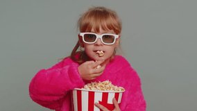 Excited young toddler school girl in 3D glasses eating popcorn, watching interesting tv serial, sport game, film, online social media movie content. Teen female child kid on studio gray background