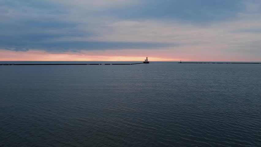 aerial flying low above water Lake Michigan towards Milwaukee breakwater light, captured at sunrise, historical landmark in Wisconsin, cinematic shot with birds on lake
