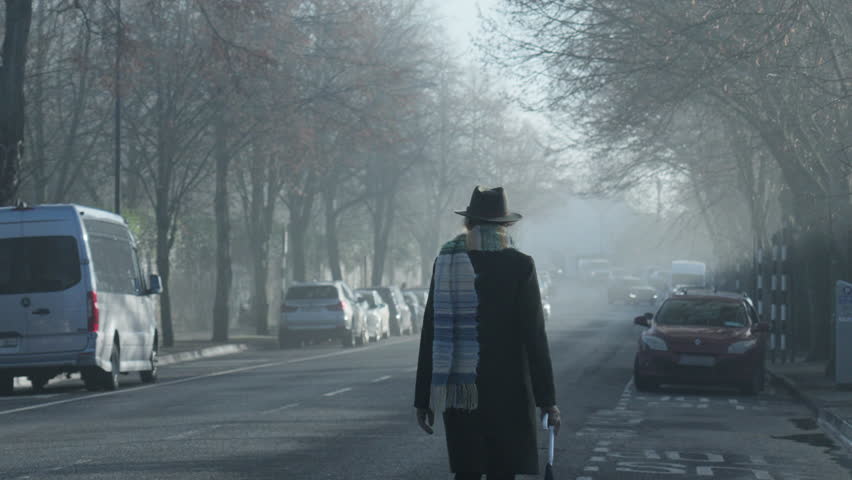 Woman walks on side of road towards incoming cars