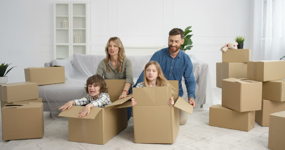 Young Caucasian parents having fun at home with kids while moving in new house. Cute small children, boy and girl sitting in carton boxes and laughing while playing with mother and father in apartment | Shutterstock HD Video #1098923749