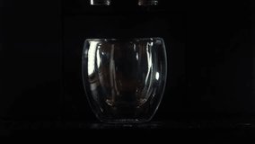 Slow motion close up 4k video with an espresso coffee in a double-walled glass cup. Fresh coffee making in an espresso machine against dark background.