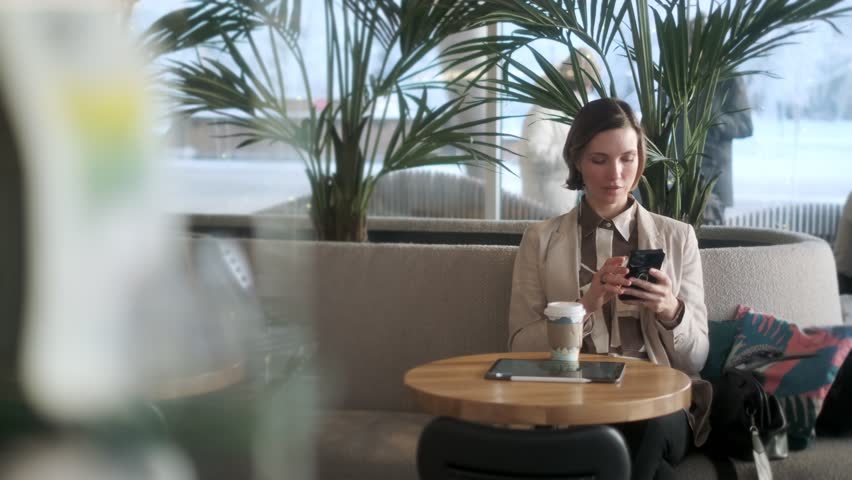 Close-up face of a confident serious business woman calling for work in a cafe using a mobile phone. A beautiful young woman with dark hair is talking on a smartphone. Close-up of a lady talking