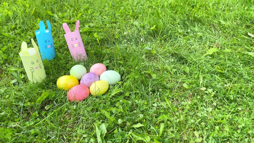 A boy with hare ears lies on the grass with colorful eggs. Egg hunting is an Easter tradition.