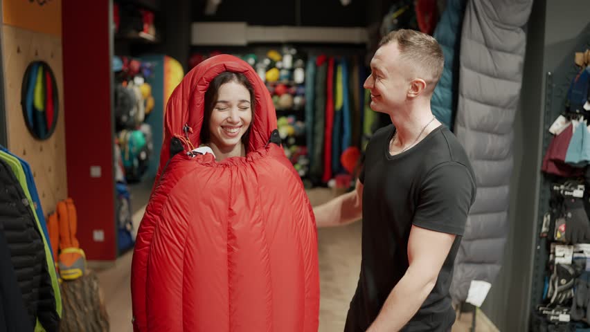 A smiling couple purchase in sportswear store, trying sleeping bag and make selfie