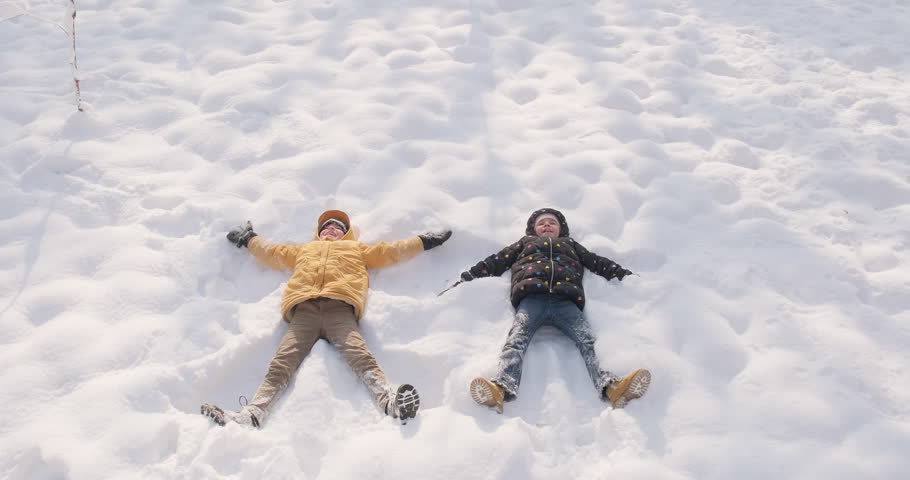 Happy kids doing snow angel. Active outdoors in winter, winter holidays, 4k slowmotion