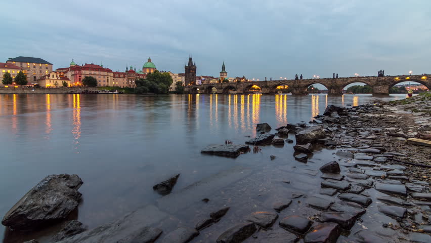 The Charles Bridge day to night transition timelapse over the Vltava River reflected in water in Prague, Czech Republic. Illuminater buildings and old town tower