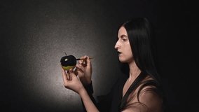 a witch with black hair paints a green apple with something black. High quality Full HD video recording