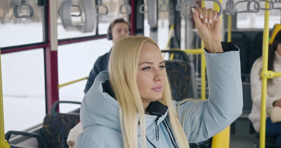 Side view of people tarveling by public transport. Young pretty woman standing. handle holding. looking in window. Concept of modern day reality, urban life and settings.