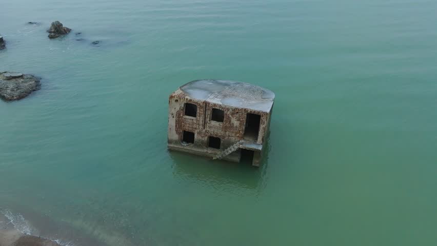 Aerial birdseye view of abandoned seaside fortification building at Karosta Northern Forts on the beach of Baltic sea (Liepaja, Latvia), waves splash, overcast day, rotating drone shot