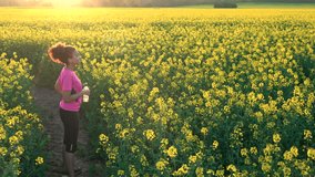 4K video clip of beautiful healthy girl teenager female young woman drinking from water bottle after running or jogging in field of yellow flowers
