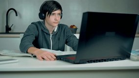 Adolescent schoolboy studying online using laptop listening web lessons in headphones. Distance education class concept during travel restrictions