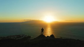 Hiking man in mountains watching sunset and horizon over beautiful ocean water landscape. Male hiker silhouette against colorful orange sky. Sun glare, sunburst. - Powered by Shutterstock - Get 15% off with code: PIKWIZARD15