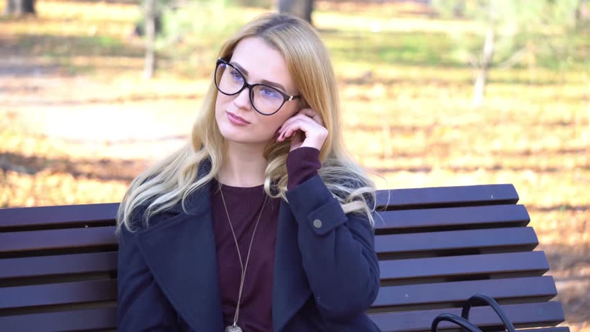 4K beautiful woman in glasses sitting on yellow leaves in the park