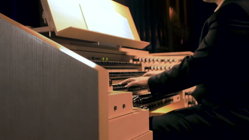 Hands playing pipe organ keyboards, sitting in suit at wood wind instrument. Fingers of organist musician performing