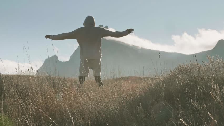 A man performs intense exercises against the background of the mountain range and mist over the peaks.