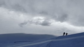 Two lonely alpinists rope team under strong wind ascending snowy slope Kazbek (Kazbegi) summit 5054m with blue sky, fast running clouds. Cruel weather conditions Caucasus mountains landscape 4k video.