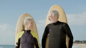 Senior couple with surfboard behind their backs on ocean shore. Medium shot of peaceful man and woman in wetsuits looking at each other and smiling at camera. Portrait, emotion, sport concept - Powered by Shutterstock - Get 15% off with code: PIKWIZARD15