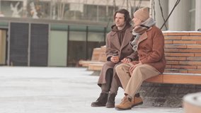 Affectionate gay couple sitting on wooden bench outdoors on winter day chatting and drinking coffee from takeaway cups - Powered by Shutterstock - Get 15% off with code: PIKWIZARD15