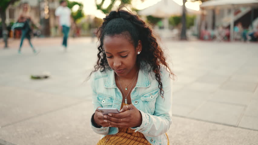 Closeup of young woman with long curly hair using a mobile phone in an urban city background. Close-up of girl sending a voice message on a smartphone | Shutterstock HD Video #1098969009