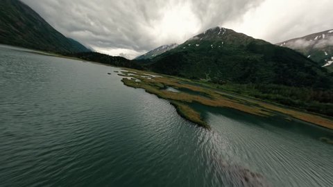 FPV drone flying over Alaskan lake with storm clouds and lush green mountain range in the background Arkivvideo