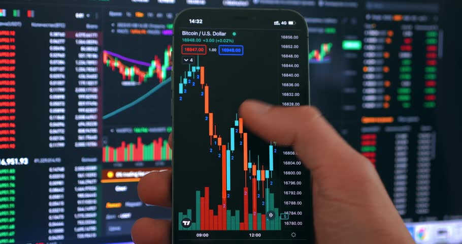 Crypto investor using mobile phone app for buying cryptocurrency in front of stock market financial screen, close up. Trader investor holding mobile phone analyzing financial crypto stock market price Royalty-Free Stock Footage #1098971957