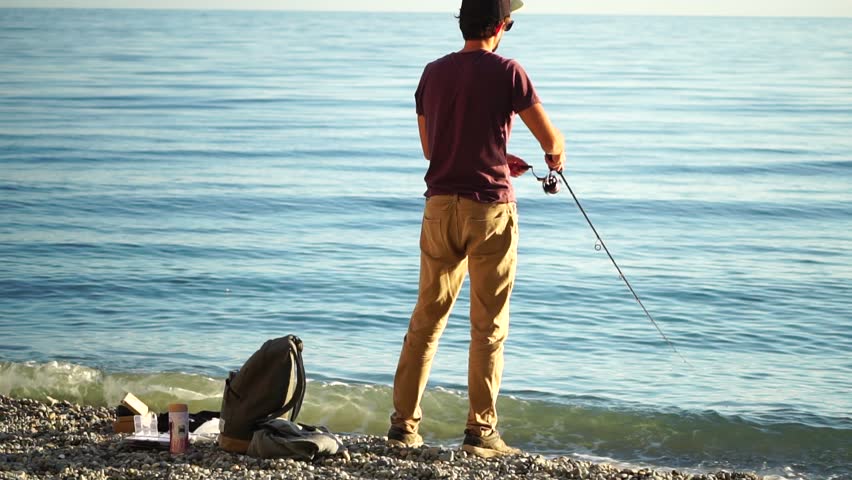 Man hobby fishing on sea tightens a fishing line reel of fish summer. Calm surface sea. Close-up of a fisherman hands twist reel with fishing line on a rod. Fishing in the sea outdoors. Slow motion.