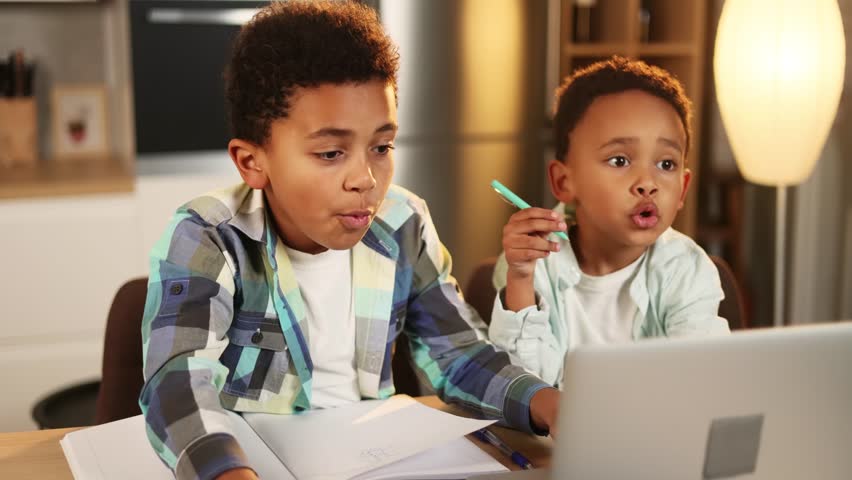 Shocked little kids brothers opening mouth looking at laptop computer screen African American children showing shock or wow emotion by unexpected good news at home kitchen