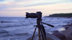 a camera on a tripod mounted on the seashore in the process of shooting waves in cold weather. the horizon line is visible, the beautiful sky and the bay. Camera on tripod Photographer take scenic vie