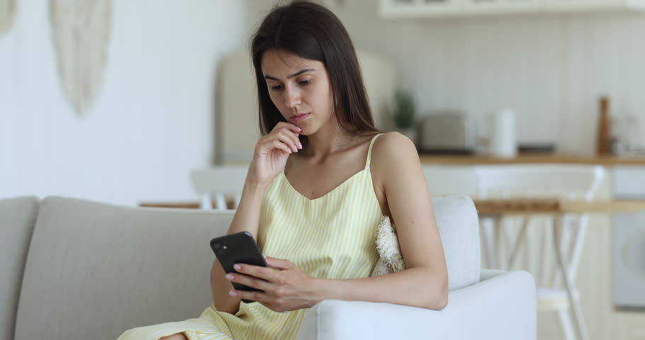 Upset young woman sits on sofa with cell phone, receive sms with bad news, read unpleasant message from boyfriend, missed or waiting for important call, staring at smartphone screen feels frustrated Royalty-Free Stock Footage #1098976555