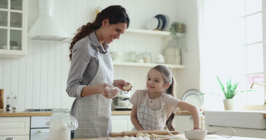 Cheerful young mother clap hands, having fun with adorable little daughter, baking together homemade biscuits, buns or pie. Loving mom, gives high five, praising her kid for help enjoy cooking at home Royalty-Free Stock Footage #1098982631