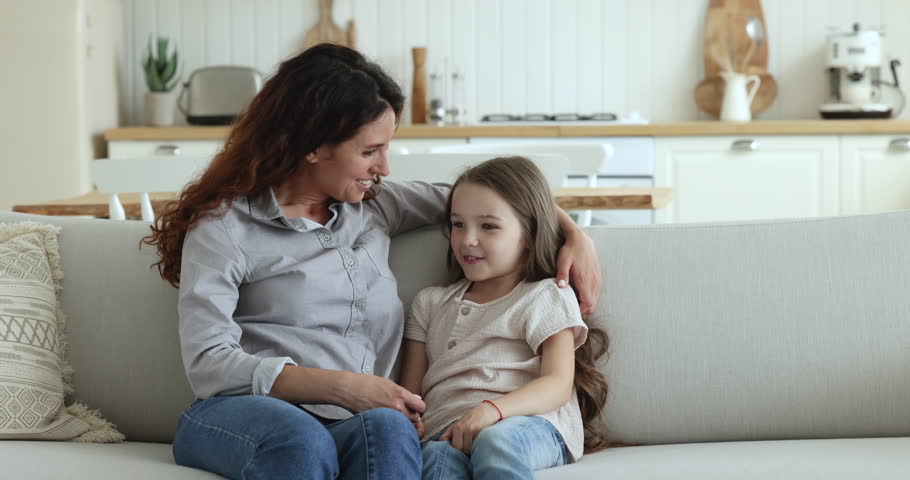 Loving Hispanic mother talks to little daughter, hugs cute small child seated together on sofa, having pleasant warm conversation, gives motherly advice express care. Trust, family ties, understanding | Shutterstock HD Video #1098982655