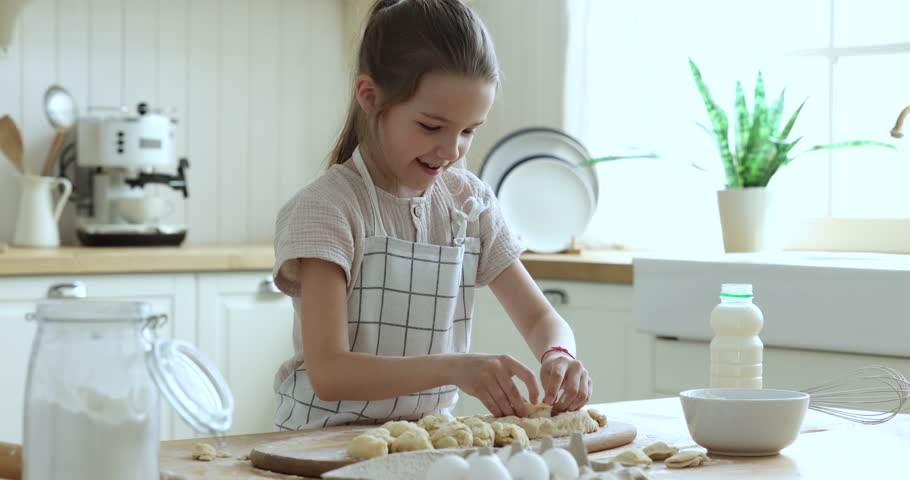 Cute little girl in apron cooking standing alone in cozy kitchen, make surprise for family on holidays, prepare dough for cookies, buns, baking homemade pastries, smile enjoy cookery process at home Royalty-Free Stock Footage #1098982729