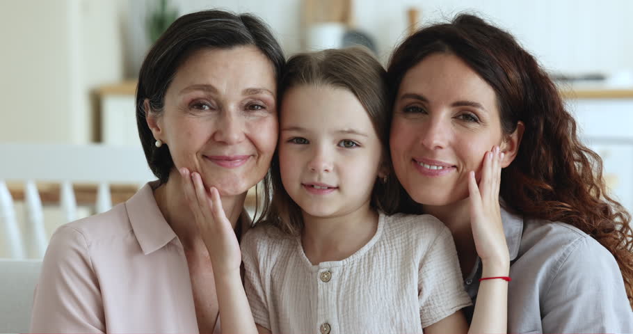 Close up portrait of multigenerational women. Little cheerful girl pose for camera with older grandma and young mum smiling staring at cam seated on sofa at home, looking happy, enjoy time together Royalty-Free Stock Footage #1098982737