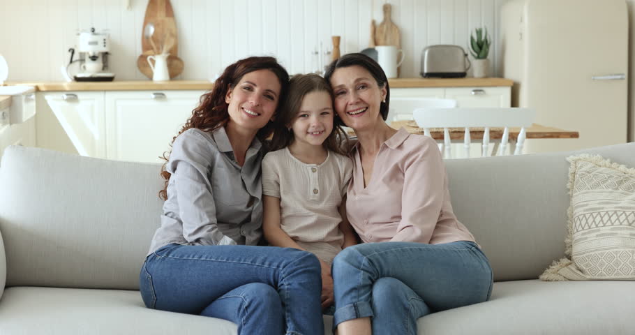 Beautiful multi generational family portrait. Older woman her grown up daughter and little granddaughter sit on sofa at home shooting for family photo, enjoy good harmonic relations and time together Royalty-Free Stock Footage #1098982747