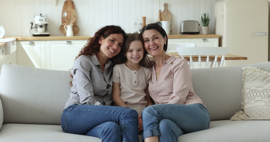 Beautiful multi generational family portrait. Older woman her grown up daughter and little granddaughter sit on sofa at home shooting for family photo, enjoy good harmonic relations and time together Royalty-Free Stock Footage #1098982747