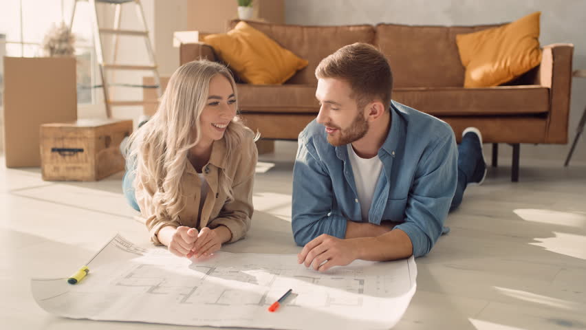 Couple Discussing Flat Plan Lying on the Floor. Couple Moving in new Home. Shot by RED Royalty-Free Stock Footage #1098984301