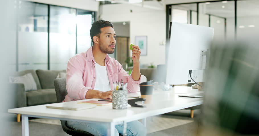 Asian man, eating apple and desk in office for lunch time snack, relax planning strategy on pc and checking phone. Businessman, reading smartphone communication and eat healthy food for nutrition