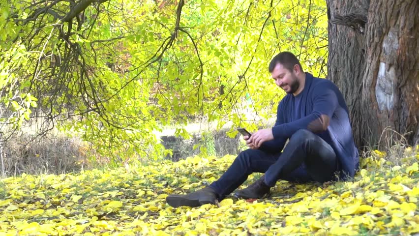 Slow Motion Man is typing a message in his phone in the autumn park 